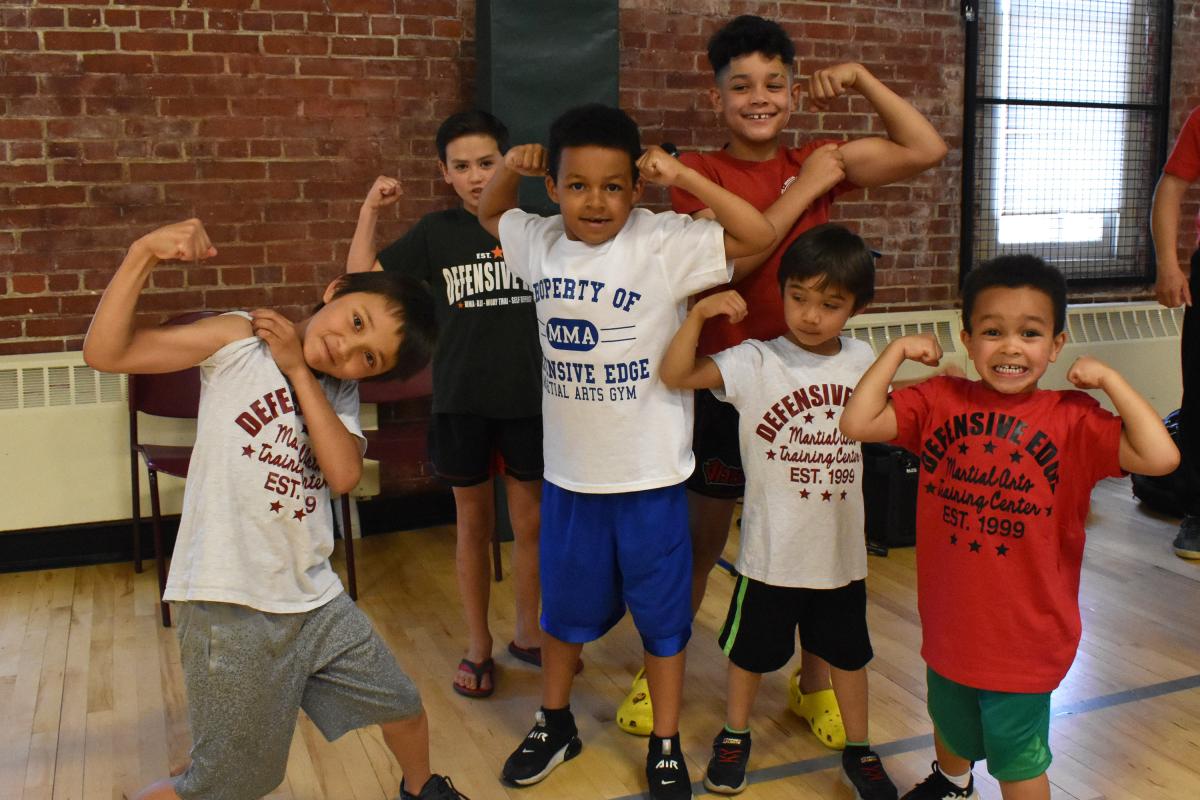 six children in Defensive Edge Martial Arts shirts flex for the camera