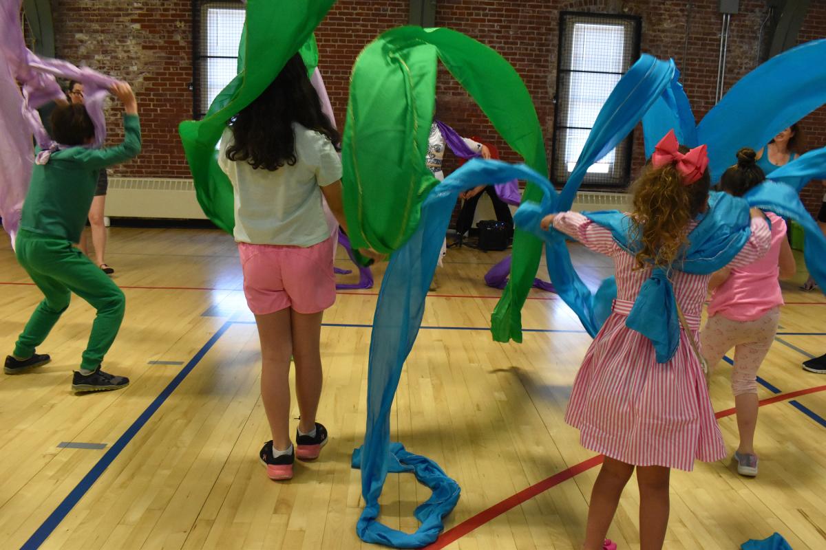 group of children dance with pink, green, and blue ribbons