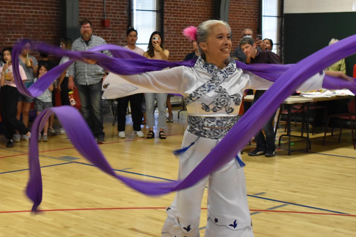 woman in white outfit dances using long purple ribbon