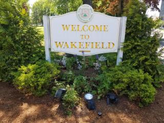 white "Welcome to Wakefield" sign in on town common surrounded by native plantings